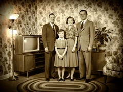 A family of four posed formally in a living room decorated in 1950s style — floral wallpaper, a wooden console television, and a braided rug — wearing period-appropriate clothing, lit by a warm tungsten floor lamp from the side, sepia-toned color grading, soft vignette edges, nostalgic mid-century photographic aesthetic.