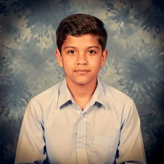 A student in a classic school yearbook portrait pose wearing a neat collared shirt, seated against a mottled blue-grey studio backdrop, soft frontal lighting from a ring flash creating even illumination across the face, slight warm tone, clean and timeless school photography aesthetic with a subtle vignette.